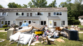 A flood damaged home has piles of damaged possessions in the lawn.