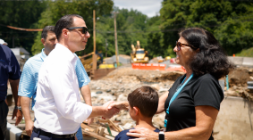 Governor Shapiro shakes hands with flood survivors in an outside area that is heavily damaged.